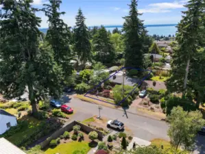 This aerial shot shows the home nestled in amongst its trees and shrubs (outlined in dark blue) across the street from the red car.  4th Avenue NW is a very quiet and friendly street in the Broadview neighborhood adjacent to Puget Sound.  Neighbors work in their gardens and walk their dogs along this street.