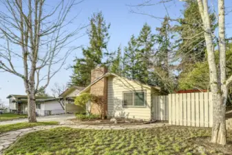 Fully fenced front yard featuring established landscaping, a flagstone pathway, and mature trees. The property boasts a newly installed roof, completed in 2026.
