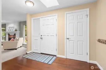 The entry features gorgeous engineered wood flooring, a large coat closet and room for more.  Not seen is the included grandfather clock. From the hallway enter the formal living space or the kitchen, lower and upper levels.