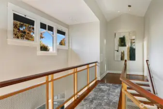 A wooden bridge framed with stainless steel mesh spans the space, overlooking a cozy first-floor reading nook on one side and a staircase on the other, and connects to two additional bedrooms