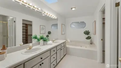 Primary bathroom with soaking tub, dual vanity, and skylight for added light.