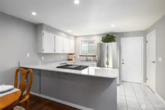 Open plan kitchen has quartz counters, gas range, stainless appliances. Door next to fridge leads to the enclosed private patio, door on the wall at right is the pantry.