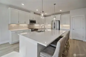 Stunning kitchen with quartz counters, oversized island, stainless steel appliances, under-cabinet lighting, and walk-in pantry.