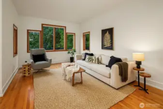 The living room offers a calm, grounded space with rich hardwood floors, clean white walls, and generous windows that frame the surrounding greenery. The layout is simple and flexible—perfect for quiet mornings with coffee or relaxed evenings with company. Natural textures and warm wood tones create a sense of comfort, while the abundant light gives the room an airy, uplifting feel. It’s a space that feels both modern and timeless, ready to adapt to any style of living.