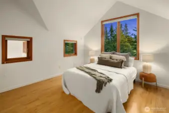The primary bedroom upstairs offers a private, light-filled retreat with vaulted ceilings and tranquil views of the surrounding trees. Generous window placement brings in both morning and evening light, creating a calming atmosphere throughout the day. The clean, minimalist design pairs beautifully with the natural wood floors, offering a peaceful space to unwind. Whether you're waking up to birdsong or winding down after a long day, this room offers a sense of quiet and connection to nature that’s hard to find.