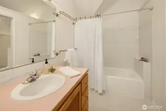 The primary bath is clean, bright, and efficiently designed, offering everything you need in a calming, understated space. A full tub and shower combo is surrounded by classic white tile, while the wide vanity provides ample counter space and storage below. Soft neutral tones and vaulted lines add to the sense of airiness, making it feel open without being oversized. It's a practical, private en suite that complements the peaceful nature of the primary suite.