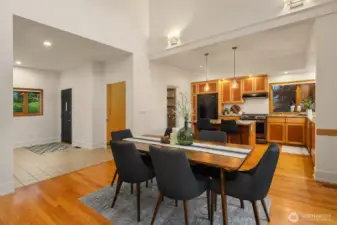 From this angle, the open flow between the entry, kitchen, and dining area is on full display—creating a welcoming layout that’s ideal for both everyday living and entertaining. The vaulted ceilings enhance the sense of space, while the warm wood tones and modern lighting provide a grounded, cohesive feel. Just off the tiled entryway, guests are naturally drawn into the heart of the home, where the kitchen island and dining table invite gathering and conversation. It’s a layout that balances openness with intimacy, offering both function and comfort.
