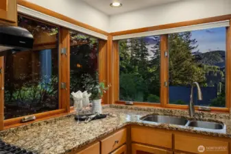 One of the standout features of this home is the kitchen's stunning corner window, offering sweeping views of the surrounding evergreens and foothills. Whether you're washing up or preparing a meal, you're treated to a peaceful, tree-filled backdrop with evening light filtering through. It’s a daily reminder of the natural beauty that surrounds 4714 Willis Street—just minutes from Lake Padden and the trail systems of Galbraith and Blanchard Mountains. This view connects the indoors with the outdoors in a way that feels distinctly Bellingham.