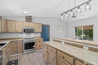 This spacious kitchen combines rustic design with smart functionality, featuring custom crossbuck cabinetry, stainless steel appliances, and ample counter space for meal prep and entertaining. A built-in microwave and air-fry capable electric range add modern convenience, while the oversized peninsula with dual-level counters and multiple outlets offers flexibility for baking, serving, or setting up a homework station. Vaulted ceilings and an open-concept layout flow effortlessly into the dining area and out to the covered patio—ideal for indoor-outdoor living in a serene, wooded setting.