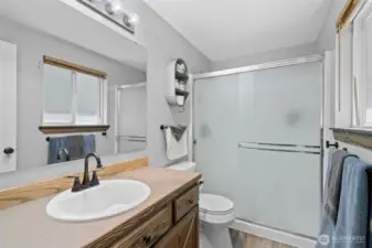 Attached 3/4 en suite bathroom features a large step-in shower with frosted glass sliding doors, stylish matte black fixtures, and a wood-accented vanity with ample storage. Natural light filters in through the window, enhancing the bright and clean aesthetic. Durable finishes and thoughtful design make this private bath both practical and inviting—perfect for everyday comfort and convenience within the primary suite.