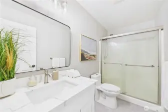 This stylish secondary bathroom features modern finishes, a quartz vanity, and a glass-enclosed shower/tub combo with privacy glass. Ideal for guests or family with a fresh, modern vibe.