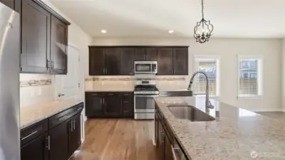 Gourmet kitchen offers a large center island, granite countertops with full-height backsplash, stainless-steel appliances and undercabinet lighting.