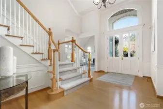 Light-filled two-story foyer featuring hardwood floors, classic millwork, and a sweeping staircase.
