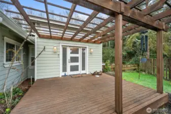 Charming pergola-covered entry deck creates a welcoming arrival space and sheltered outdoor sitting area surrounded by lush greenery.