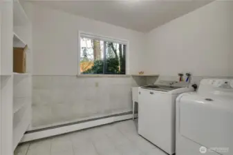 Spacious laundry area with additional storage and workspace for everyday convenience. Equipped with a washer, dryer, utility sink and tile flooring and partial wall.