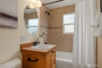 The main floor bath (one of two) features a shaker design wood vanity and a tiled bath surround.