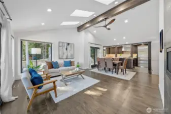 Stunning open-concept living space is filled in natural light, thanks to strategically placed skylights that enhance the airy feel of the vaulted ceiling. A sleek, modern ceiling fan complements the exposed wood beam, adding a stylish touch to the bright and inviting living area.