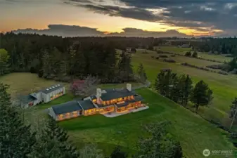 Dramatic sunset aerial showcasing the illuminated estate across expansive lawns, highlighting architectural scale and exceptional privacy within 63± acres.