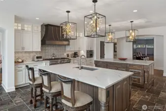 Spacious chef’s kitchen featuring dual oversized islands with marble countertops, custom wood cabinetry, farmhouse sink, and designer pendant lighting.