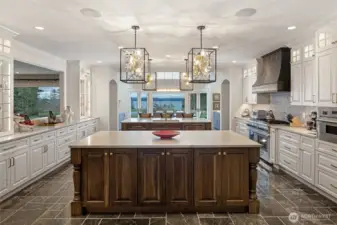 Open-concept gourmet kitchen with professional-grade range, custom vent hood, extensive cabinetry, and framed San Juan Channel views through French doors.