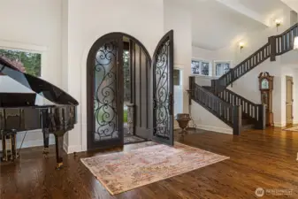 Impressive arched iron and glass entry doors open to soaring ceilings, rich hardwood floors, and a dramatic staircase with custom railing.