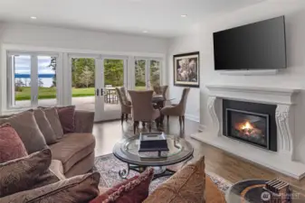 Inviting living space with gas fireplace, custom mantel, rich hardwood floors, and French doors opening to terrace with sweeping water views.