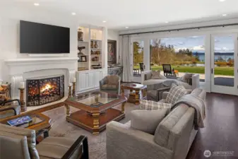 Inviting great room featuring gas fireplace with custom surround, built-in shelving, and French doors opening to patio and waterfront grounds.