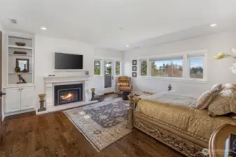 Luxurious primary suite offering fireplace, hardwood floors, and expansive windows capturing serene island and water vistas.