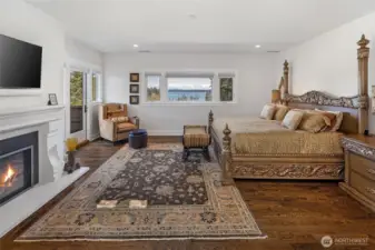 Spacious primary suite featuring gas fireplace, hardwood floors, private deck access, and expansive windows capturing panoramic San Juan Channel views.