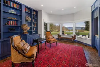 Refined library with custom built-ins, rich blue cabinetry, hardwood flooring, and bay windows overlooking manicured lawn and San Juan Channel views.