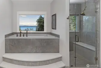Spa-inspired primary bath with elevated soaking tub framed by picture window, marble tile surround, and sweeping water views toward Mount Baker.