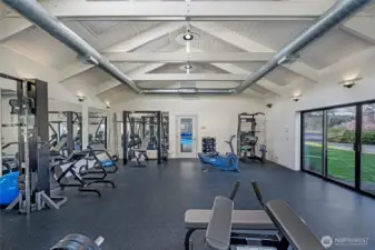 Private fitness studio with vaulted ceilings, exposed beams, full gym equipment, rubberized flooring, and sliding doors to exterior grounds.