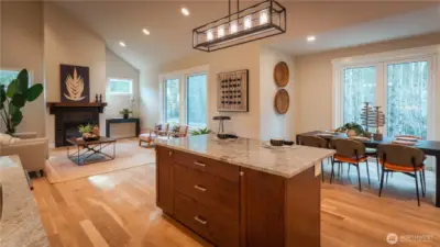 This beautifully designed open-concept space showcases a seamless flow between the kitchen and great room. Vaulted ceilings enhance the sense of volume, while large windows fill the room with natural light. The expansive island offers generous prep space and seating, making it the true centerpiece for gathering and entertaining. The living area is anchored by a cozy fireplace, creating a warm and inviting atmosphere.