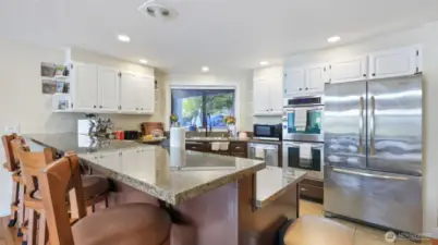 Large kitchen with eating bar, double ovens, dishwasher, microwave and cooktop.