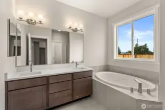 Primary bathroom has a double vanity with undermount dual sinks, tile floor, quartz countertops and a soaking tub with tile surround.