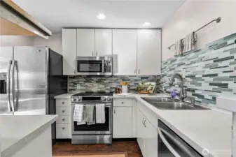 The kitchen is airy, with stainless steel appliances, glass tile backsplash and white wood cabinets