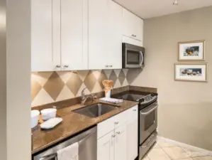 The kitchen is crisp and inviting, featuring white cabinetry, stainless appliances and slab countertops.