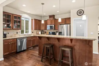Spacious kitchen with granite countertops, rich cabinetry, stainless steel appliances, and a large island with seating and abundant storage on the opposite side.