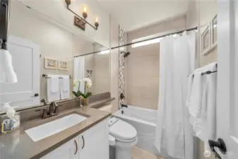 Guest bath with Quartz counters, upgraded fixtures & lighting, oversized tub w/ tile surround & tile floors.