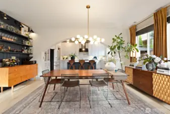 Another view of the dining room, showcasing the stunning architectural arch that elegantly frames the kitchen beyond. This thoughtfully curated space features a custom shiplap bar with accent lighting and a brass foot rail from Paxton Hardware—both stylish and functional. A mid-century modern chandelier from West Elm anchors the dining area, complemented by motorized blinds, upgraded window casings, and designer sconces from Shades of Light. Throughout the main living spaces, you’ll find luxury vinyl plank flooring, sleek Enerlite Elite Series gold switches and outlets, antique gold door hardware, and crisp 6-inch baseboards—all combining to create a seamless blend of form and function.