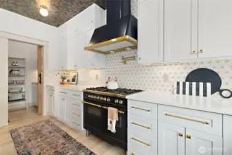 This designer kitchen is as functional as it is beautiful, anchored by the statement-making ILVE 36-inch Nostalgie dual fuel range with five sealed brass burners and a 3 cu. ft. oven—offering premium performance with vintage-inspired flair. Above, the ILVE Majestic wall-mounted range hood delivers 600 CFM of ventilation power, four fan speeds, warming lights, and a sleek auto-off function. A shimmering marble mosaic backsplash with glittery gold grout sets the stage for high-end finishes, including a Kraus brushed gold pot-filler and faucet. Cabinet hardware from Rejuvenation completes the look, featuring aged brass Emerson drawer pulls paired with matching cabinet knobs for a warm, cohesive finish that elevates the entire space.