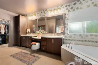 The expansive primary bathroom is both luxurious and practical, offering a spa-like layout with room to truly unwind. It features a large soaking tub beneath a frosted window for privacy and natural light, a walk-in shower, and a separate water closet with a stylish feature wall and added shelving. Dual vanities with updated lighting, new faucets, and elegant brass hardware provide plenty of space for morning routines. Rich cabinetry, a built-in makeup vanity, and a convenient linen closet complete this beautifully appointed retreat.