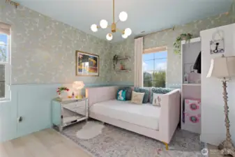 This dreamy, color-drenched bedroom is filled with thoughtful touches and stylish upgrades. High-quality floral wallpaper pairs perfectly with custom wainscoting, adding texture and visual interest to the space. A modern chandelier and integrated LED lighting provide a warm glow, while built-in closet shelving maximizes storage. With a serene palette and elegant finishes, this room feels both playful and peaceful—perfect for rest, reading, or creativity.