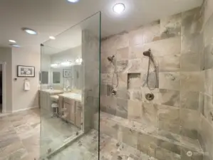 Spacious walk-in shower with ramp, two hand-held shower heads, product cubby and bench.