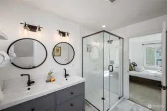 En suite bathroom with a walk-in tile shower, dual sinks, sleek black fixtures, and tile floors.