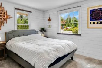 Bright primary bedroom with shiplap walls and large windows.
