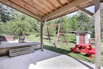 View of covered patio and deck from living room doors. Hot tub & swing set stay, pump house on your right.