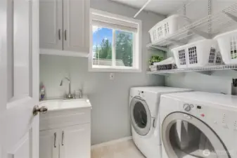 Laundry room is spacious and features front load washer and dryer that convey. Shelving & soaking sink with cabinet storage