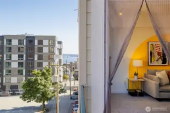 From the balcony looking south, enjoy peek-a-boo views of Elliott Bay and the Puget Sound, along with a glimpse into the vibrant living room.
