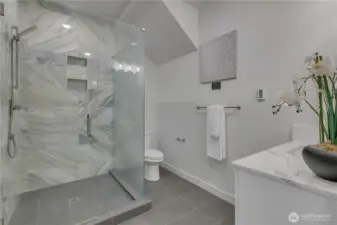Unit B main floor 3/4 bathroom with marble surround double-wide walk-in shower, quartz  vanity counter & tile flooring.
